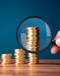 Magnifying glass examining stacks of coins that are increasingly taller