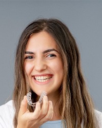 a smiling young woman holding Invisalign aligners