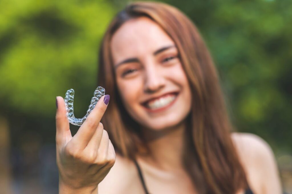 A smiling woman holding an Invisalign aligner.